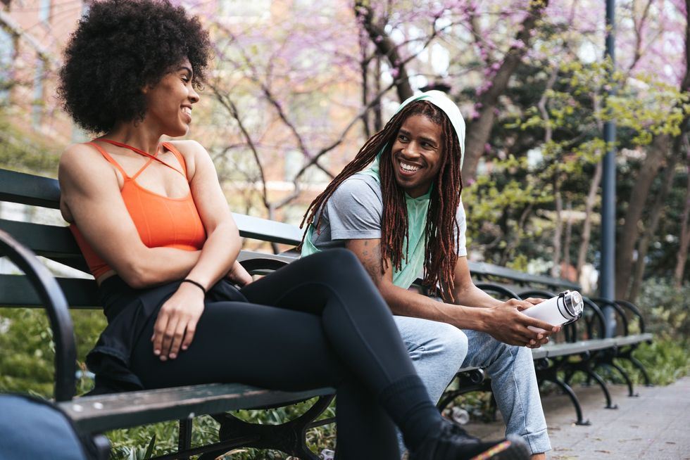 young-woman-and-young-man-sitting-on-a-park-bench-taking-a-break-from-exercising-sharing-a-laugh-conversation