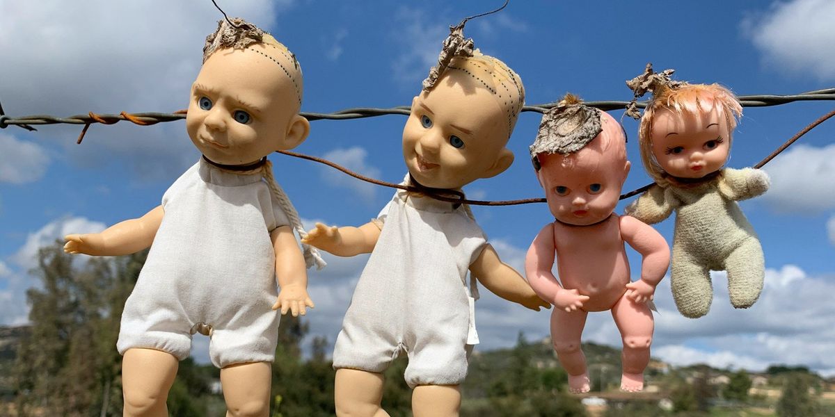 Four mistreated baby dolls are hung by barb wire