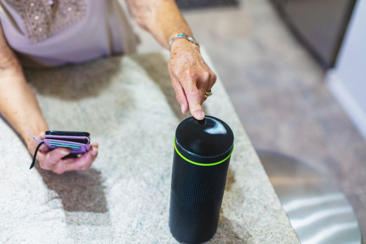 a photo of an elderly woman on her smartphone activating a smart speaker