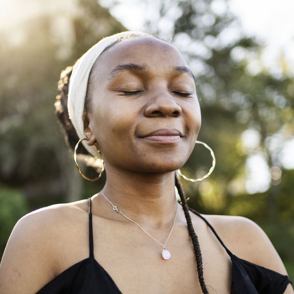 stylish-Black-woman-in-head-wrap-standing-with-eyes-closed-and-smiling-outside-in-the-sun