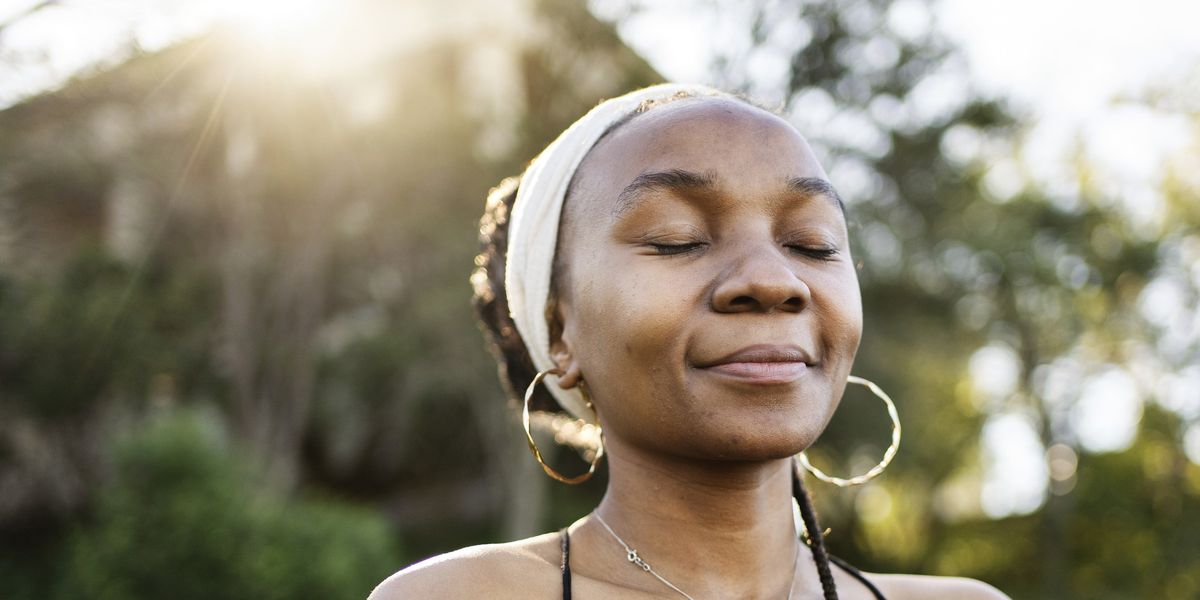stylish-Black-woman-in-head-wrap-standing-with-eyes-closed-and-smiling-outside-in-the-sun