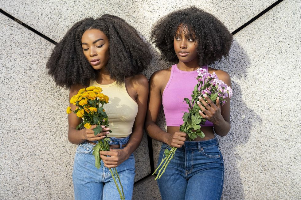young-woman-with-female-friend-leaning-on-wall-holding-boquets-of-flowers