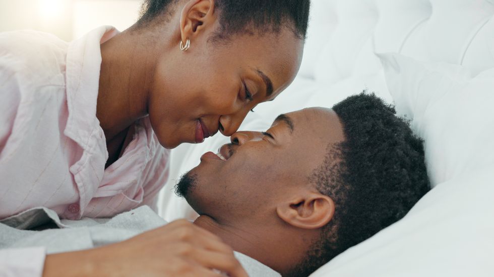a-Black-couple-laying-in-bed-together-with-woman-leaning-over-to-touch-noses-with-the-man