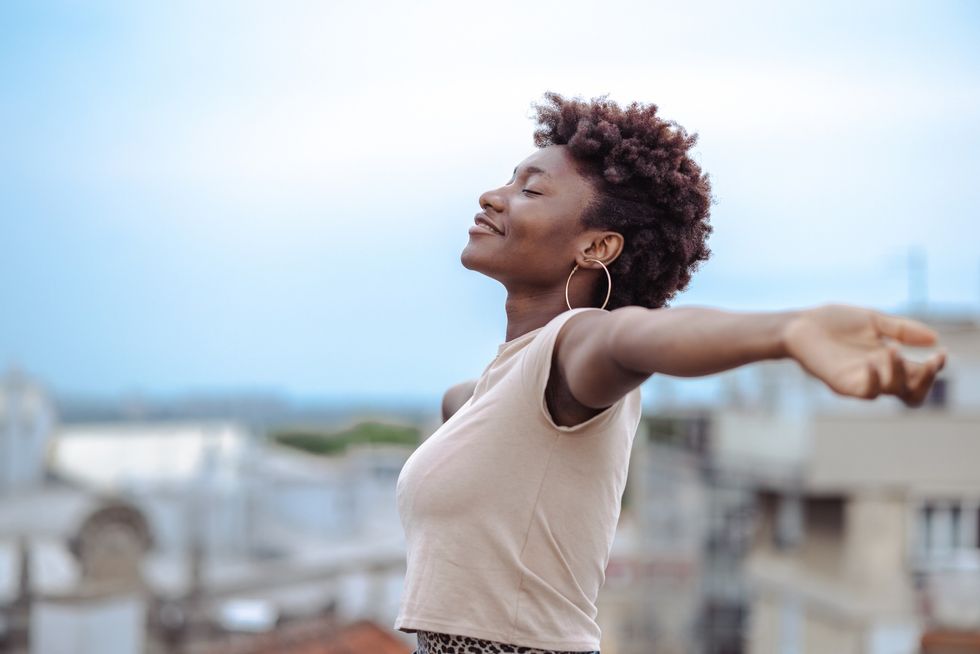A-young-African-American-woman-standing-on-the-rooftop-with-her-arms-open-and-eyes-closed