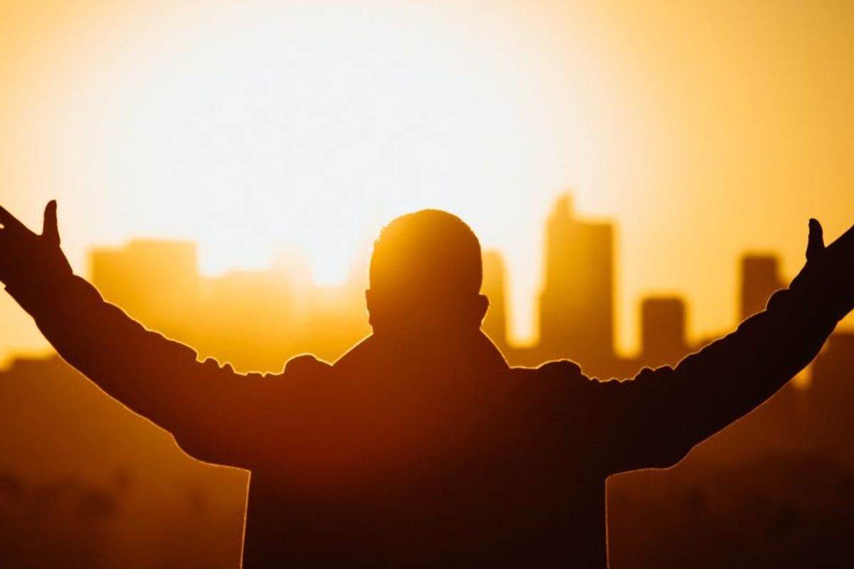 man standing with his arms raised, facing the rising sun