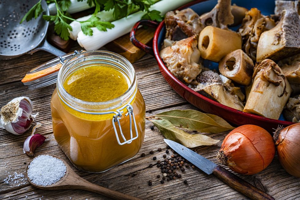 Bone-broth-in-an-open-jar-surrounded-by-ingredients-rustic-background