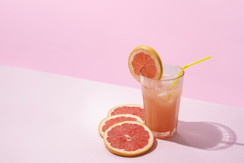 Grapefruit-juice-in-a-glass-with-a-straw-against-pink-background-grapefruit-slices-decorating-the-glass