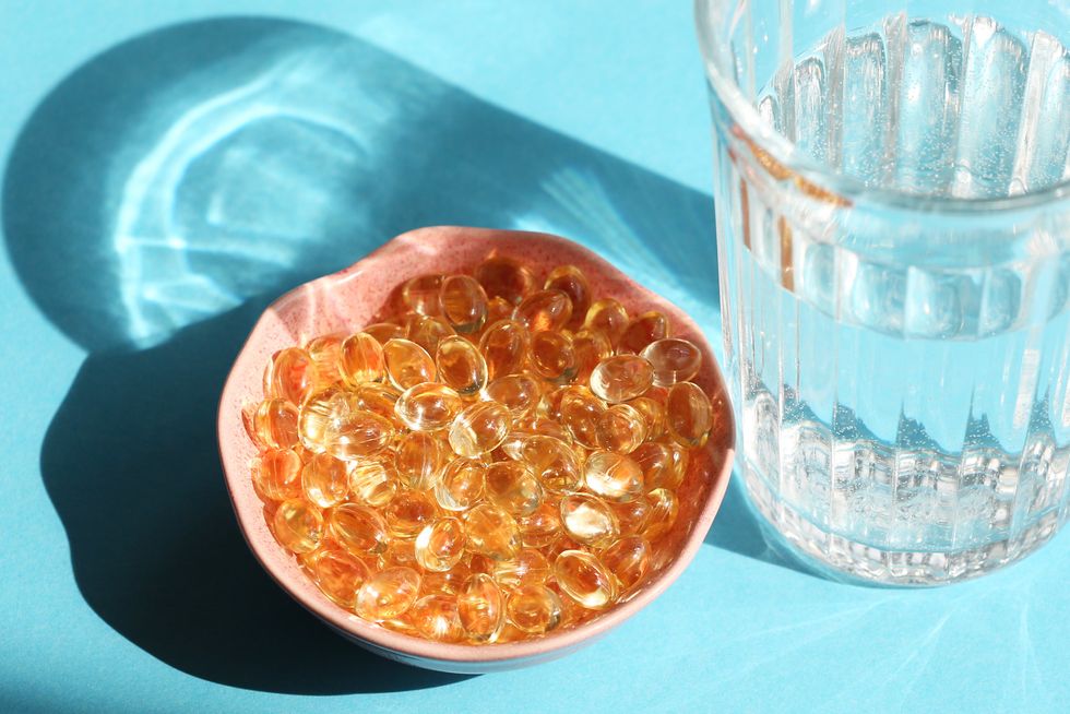 Orange-vitamin-supplements-in-a-bowl-near-a-glass-of-water-against-light-blue-background