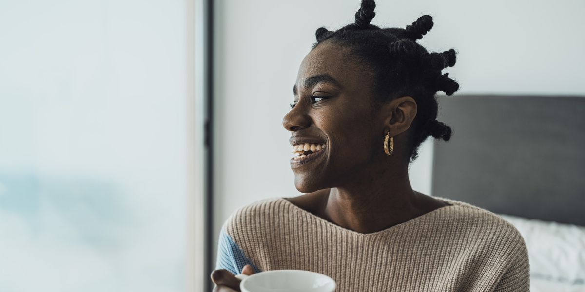 young-woman-smiling-with-afro-hairstyle-sitting-on-bed-and-drinking-coffee
