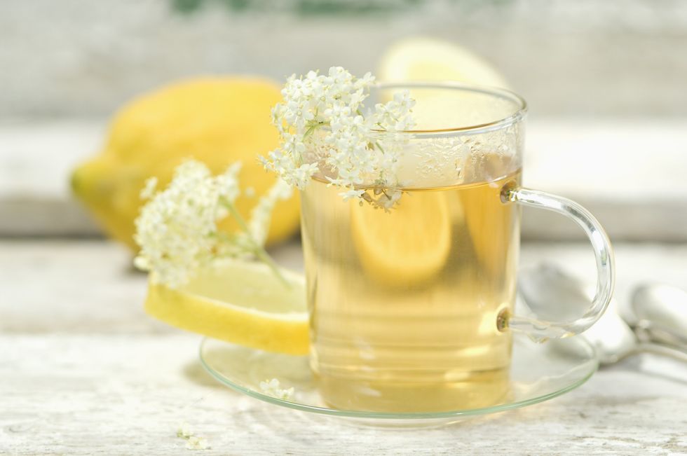 Close-up-of-warm-beverage-in-glass-teacup-saucer-set-with-white-flowers-and-lemons-in-background