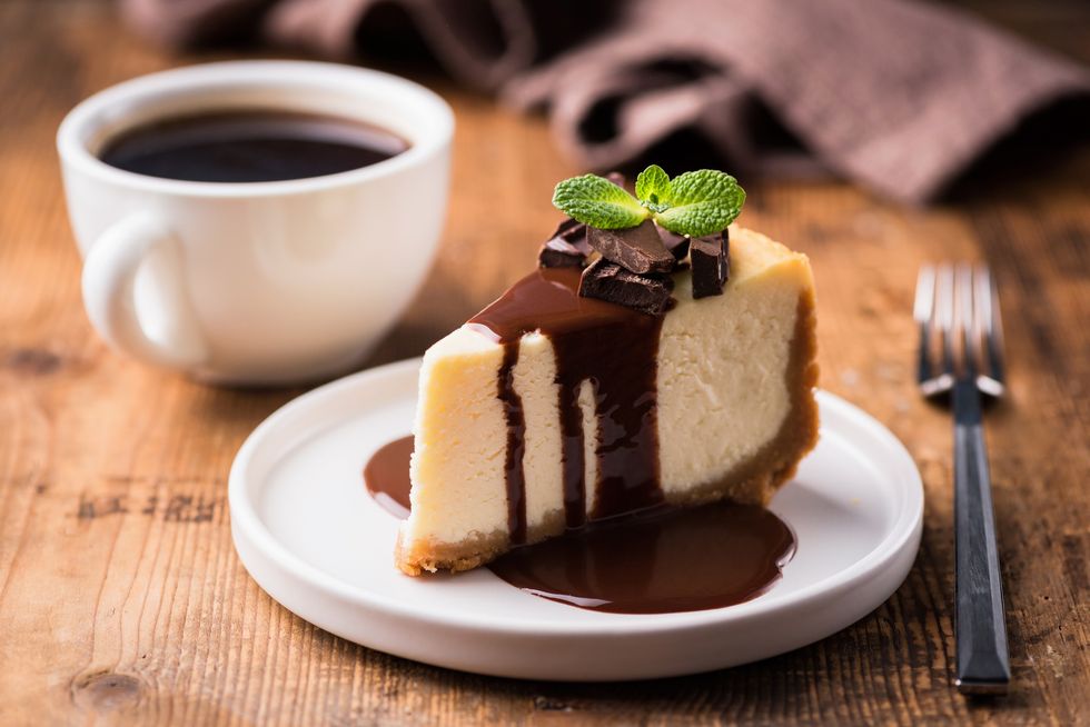 A-slice-of-cheesecake-with-chocolate-sauce-and-shavings-and-a-cup-of-black-coffee-on-the-side