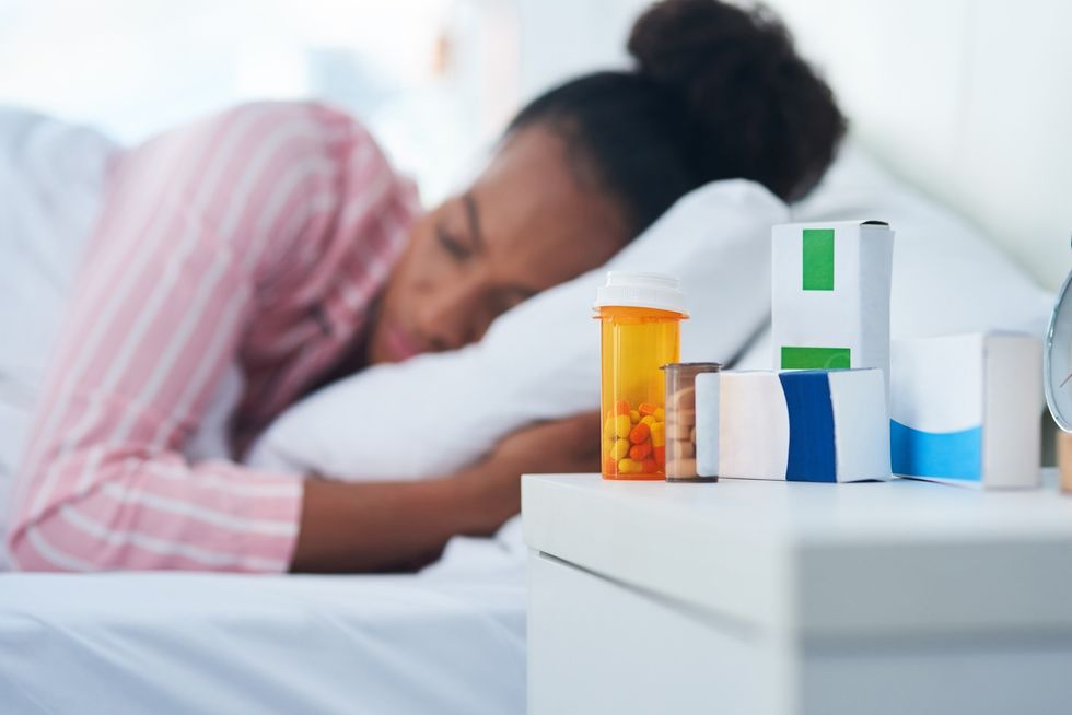 Sleeping-Black-woman-out-of-focus-behind-pill-containers-on-her-nightstand