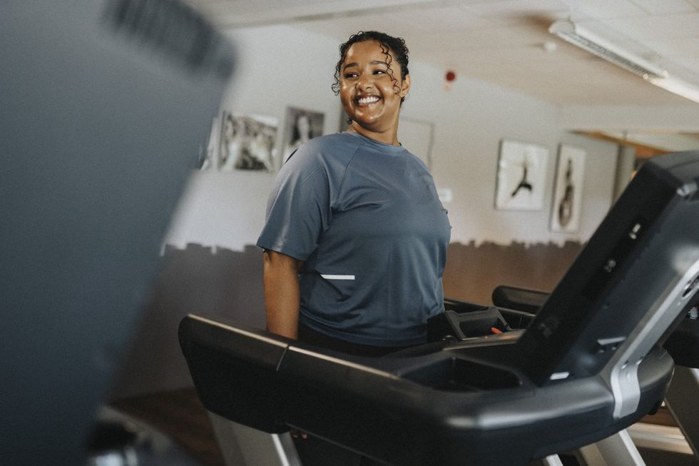 Smiling-curly-haired-woman-pausing-on-her-treadmill