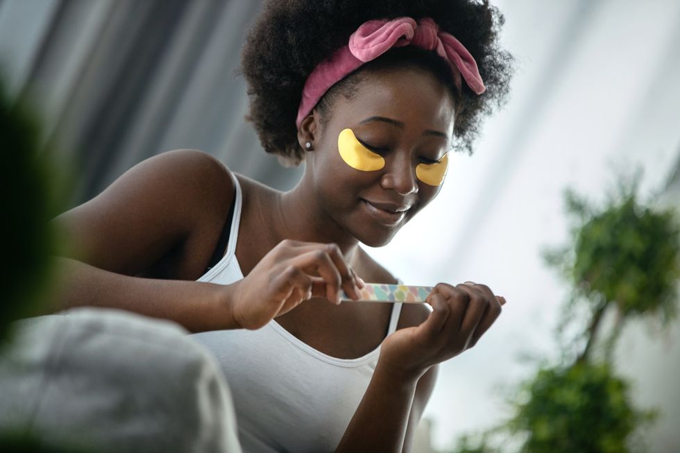 Black-woman-enjoying-a-tranquil-spa-moment-at-home-wearing-gold-eye-patches-using-a-nail-file