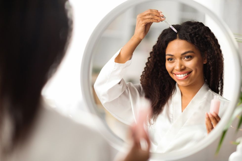 Cheerful-Black-woman-applying-product-to-her-scalp-in-the-mirror