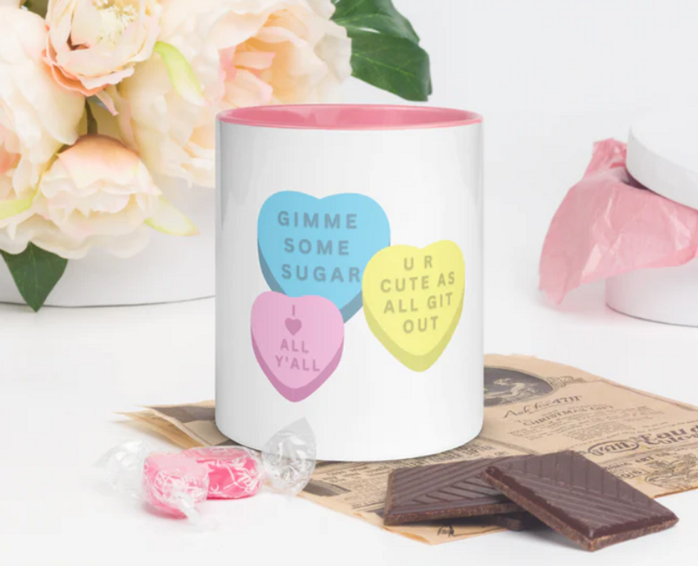 A white coffee mug with yellow, pink and blue conversation hearts pictured on it.