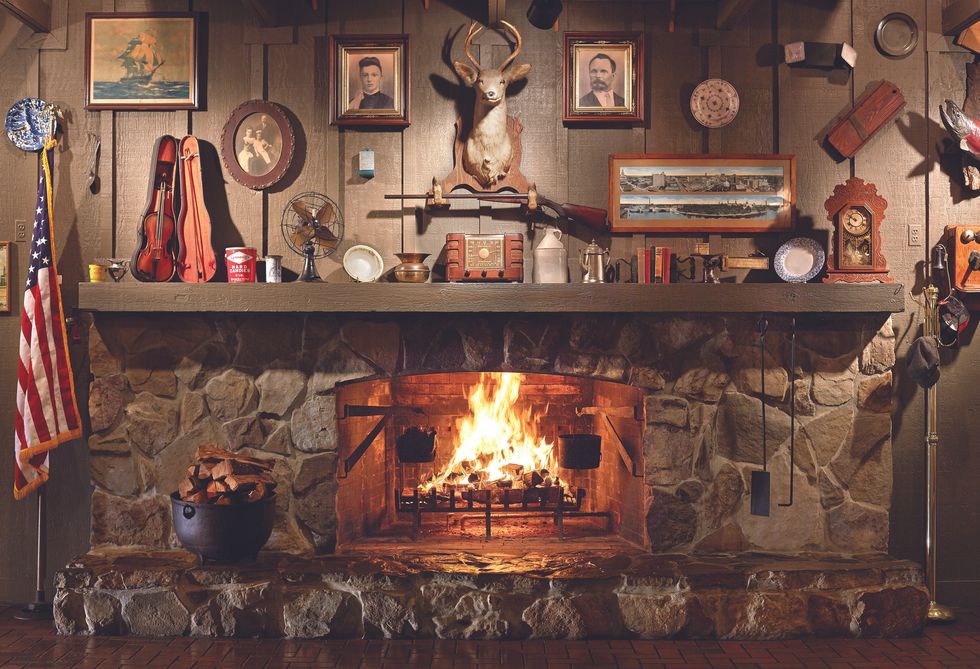 A lit stone fireplace with an assortment of items, including a deer head and portrait, hanging above it as decor inside a Cracker Barrel restuarant.