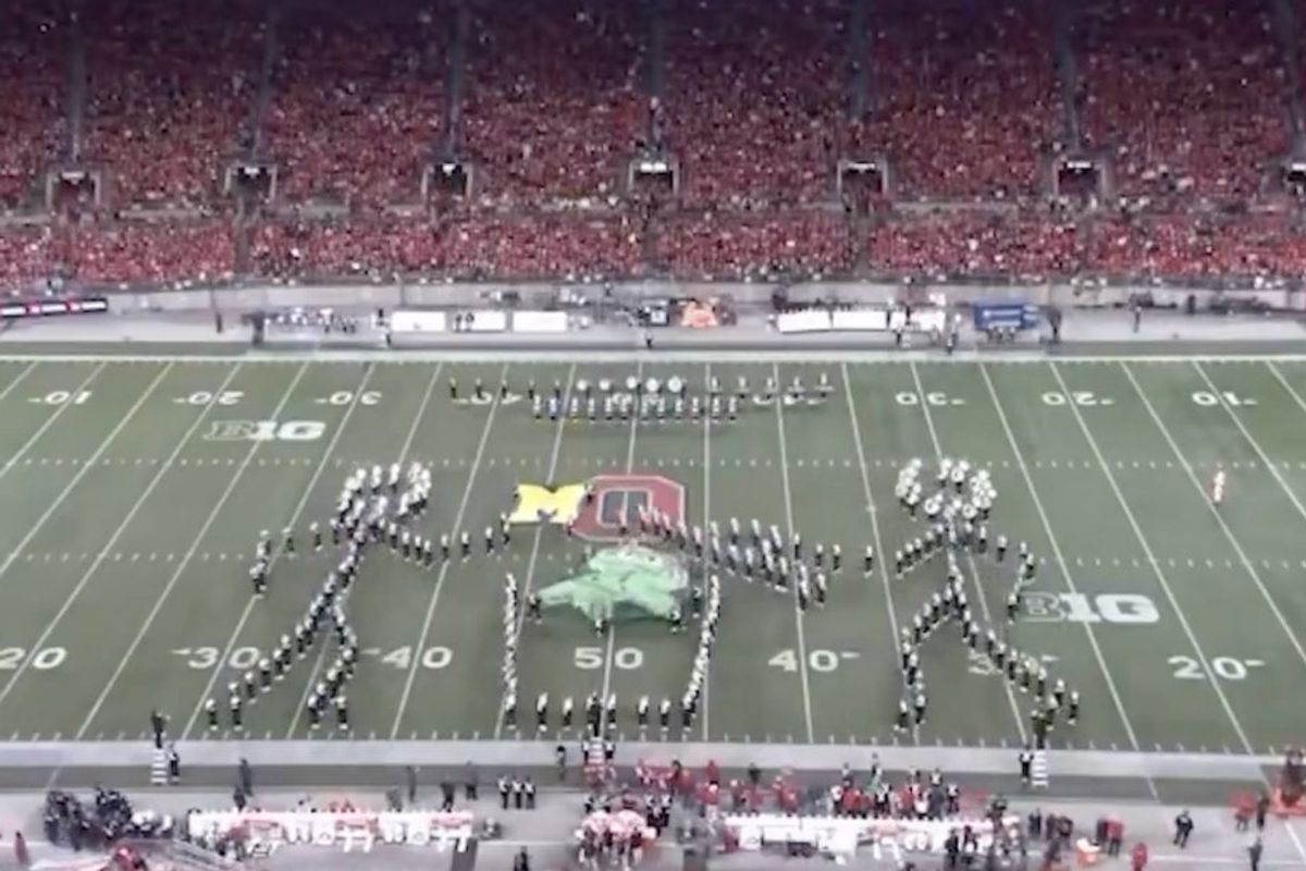 marching band members arranged to look like a person taking the lid off at trash can and another person throwing the Michigan flag into it