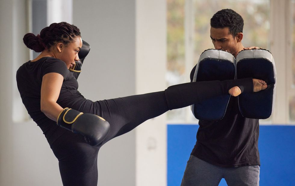 Black-woman-performing-a-kick-at-her-trainer-while-kickboxing