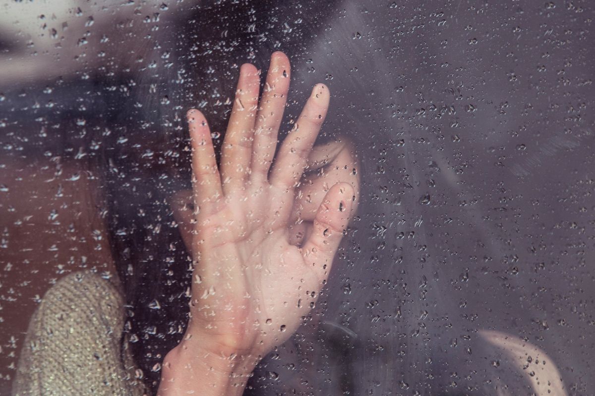 woman crying with her hand on a rainy window 