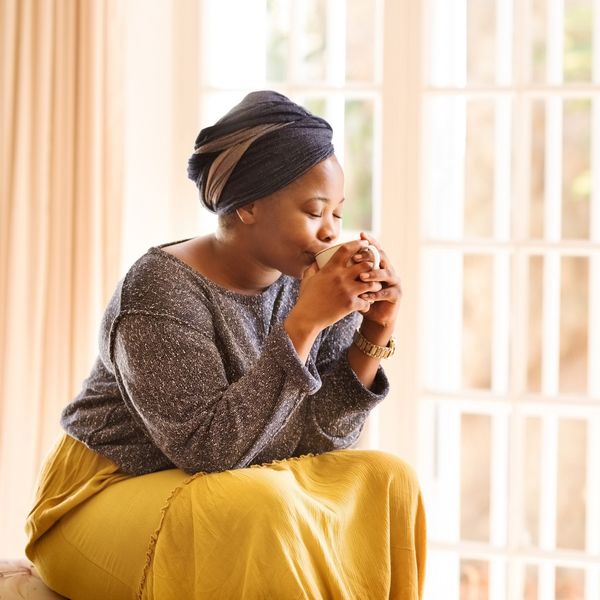Young-woman-sitting-in-bedroom-drinking-hot-beverage-in-peace