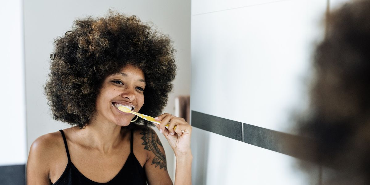 Multiracial-woman-brushing-her-teeth-in-bathroom-mirror