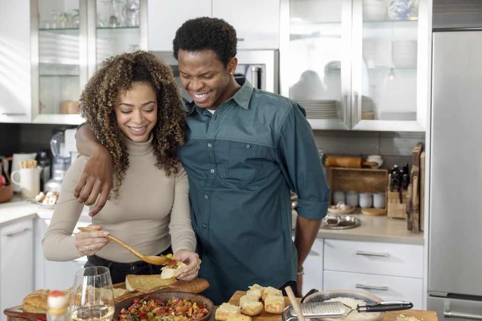 Woman-preparing-food-on-toasted-bread-while-partner-holds-her-shoulders