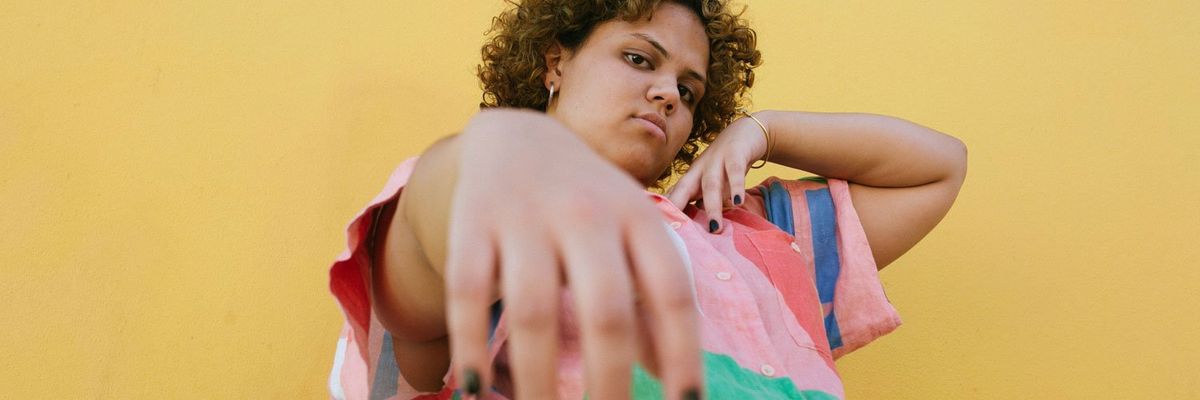 Portrait of a vibrant Latin woman in a colorful shirt against a sunny yellow backdrop.