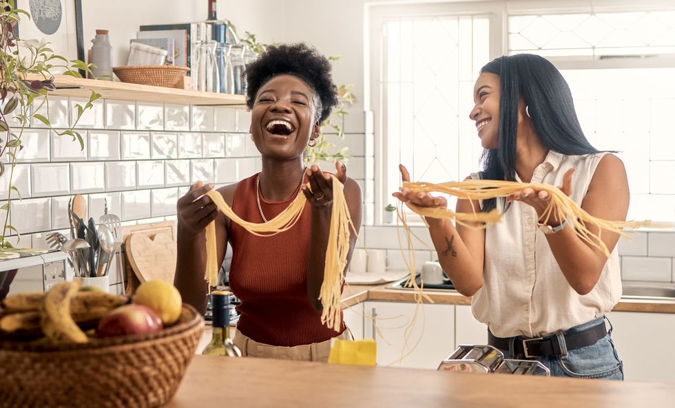 Two-friends-laughing-making-fresh-pasta-in-kitchen-at-home