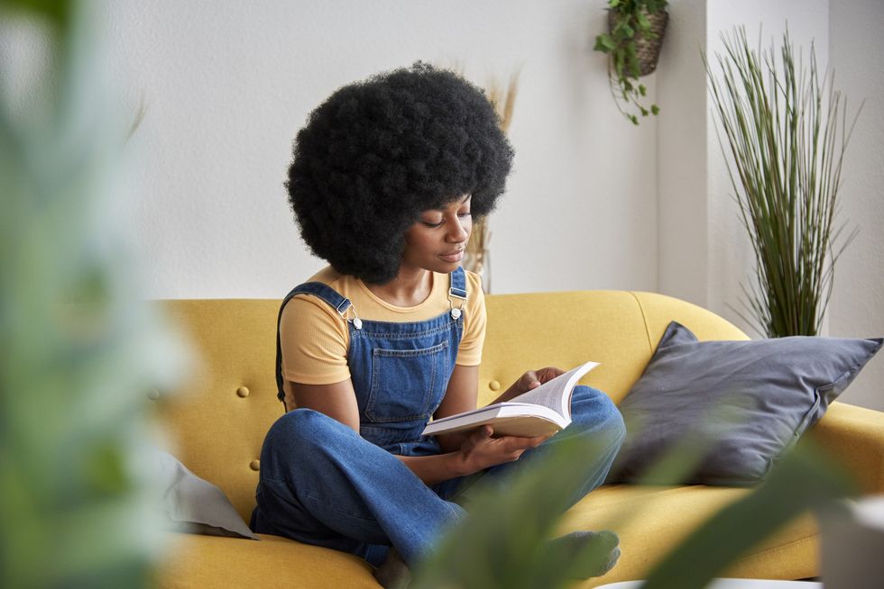 Black-woman-sitting-cross-legged-on-a-yellow-couch-reading-a-book