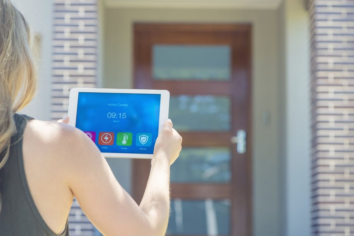 a photo of a woman using a tablet to control her smart home while standing outside her front door.