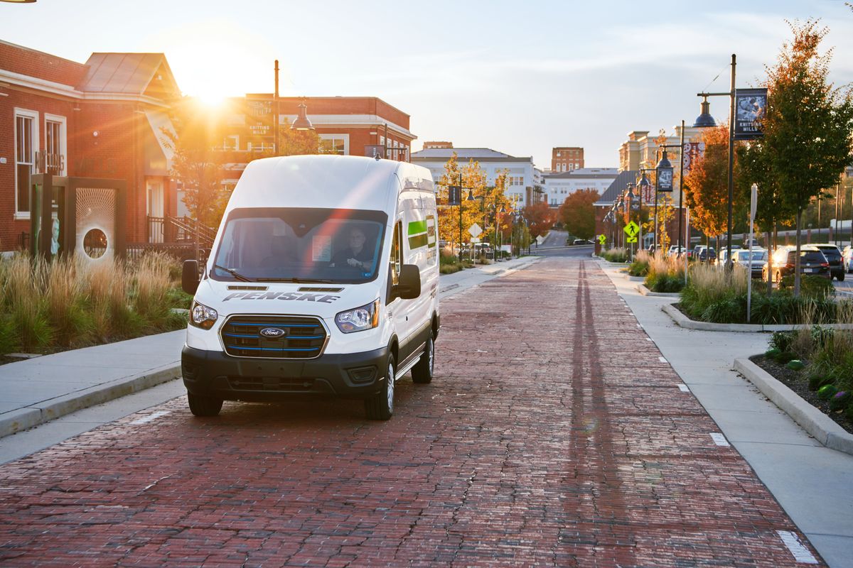 An Penske electric cargo van drives up a brick road in the city.