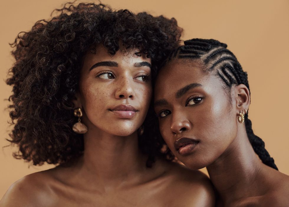 Portrait-of-two-pretty-Black-women-wearing-their-natural-hair-against-brown-background