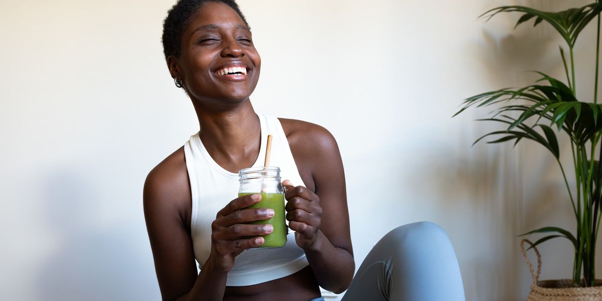 Happy-young-Black-woman-in-her-yoga-pants-drinking-green-juice-wellness-aesthetic