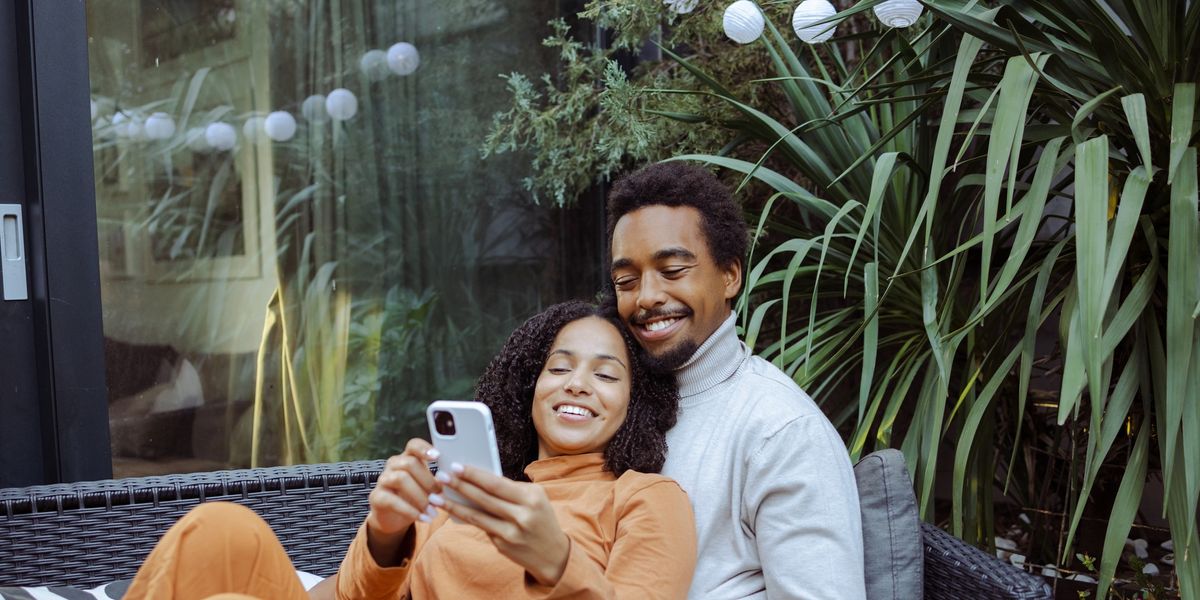 Happy-young-African-American-couple-enjoying-leisure-time-together-while-scrolling-phone-dating-apps