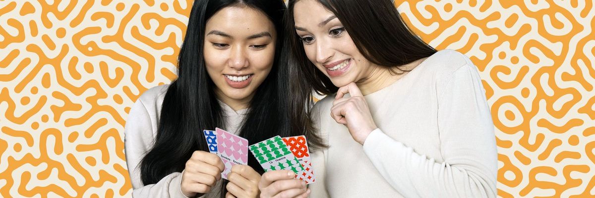 Two Latina women happily playing a board game, holding cards in their hands and enjoying the moment.