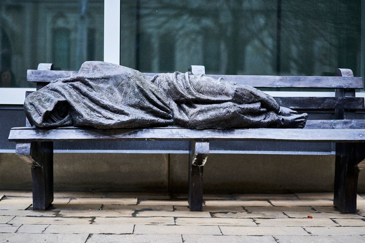 statue of man wrapped in cloak lying on a bench