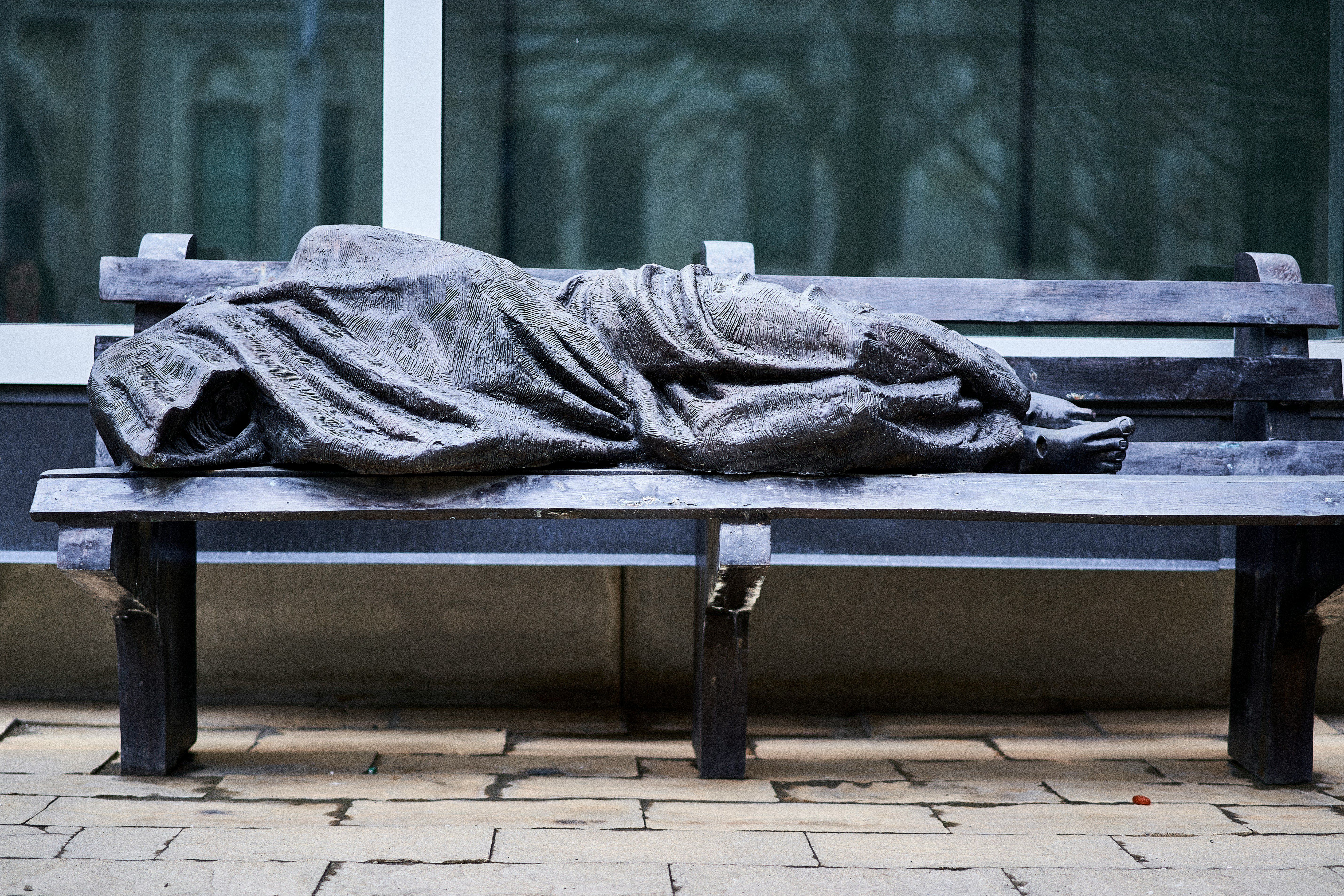statue of man wrapped in cloak lying on a bench