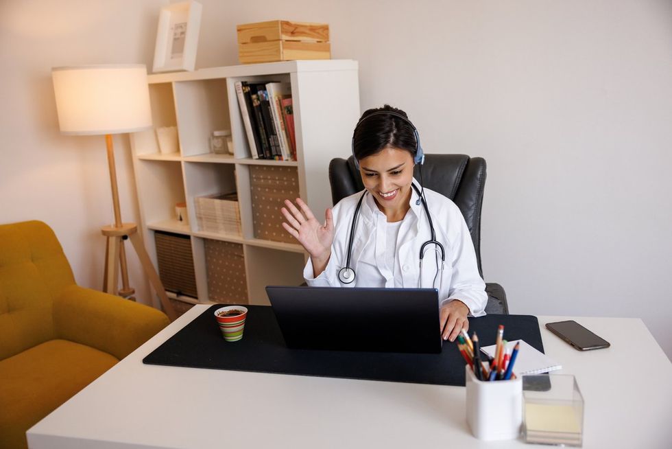 Female doctor waving and talking with colleagues through a video call on laptop stock photo