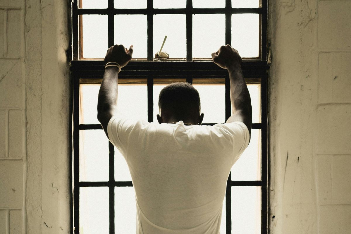 man with his back to camera places arms on barred jail window