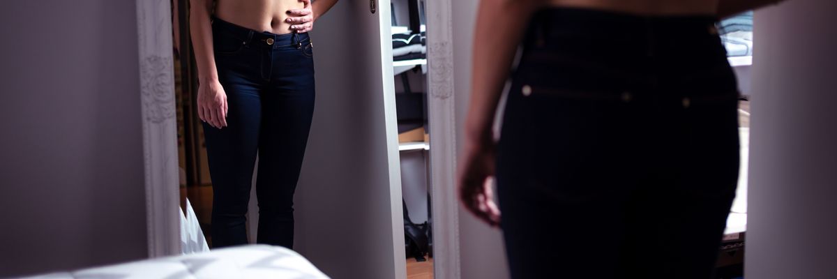 woman in black pants and black bra looks at her image in a mirror 