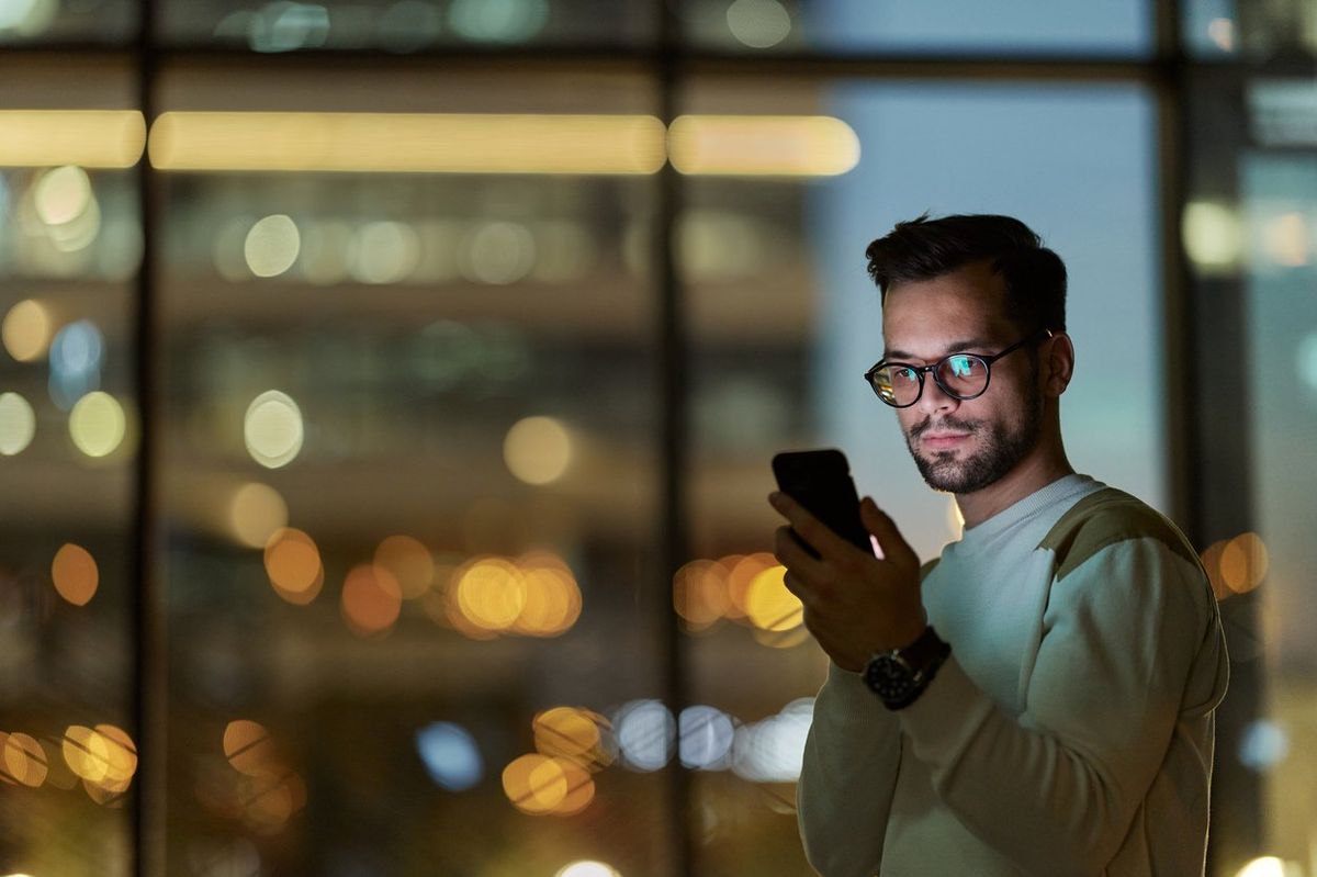 Young serious man reading a text message on smart phone in the dark.