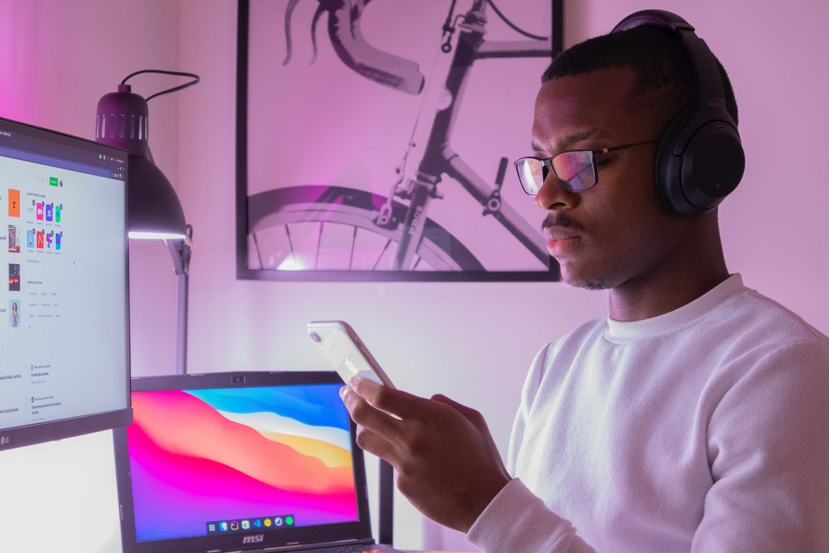 man at the computer looking at his phone with headphones on