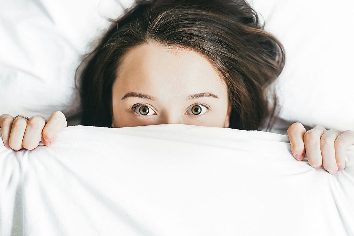 a woman holds a bedsheet up to her eyes