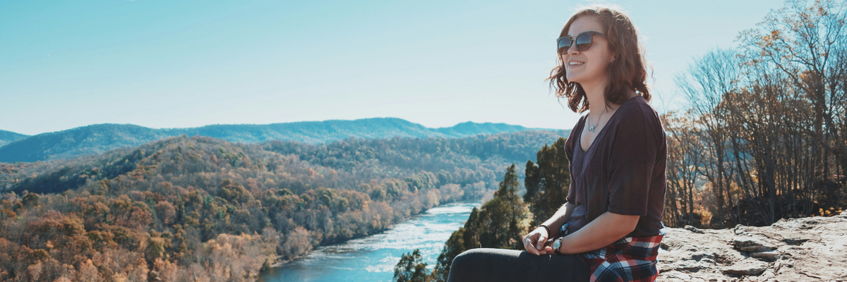 A woman enjoys a stunning view of river, forest, and nature from her rocky perch