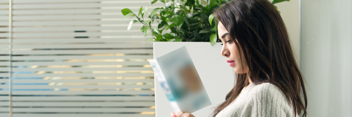  A Latina woman sits in a doctor's office, holding and reading a health pamphlet.