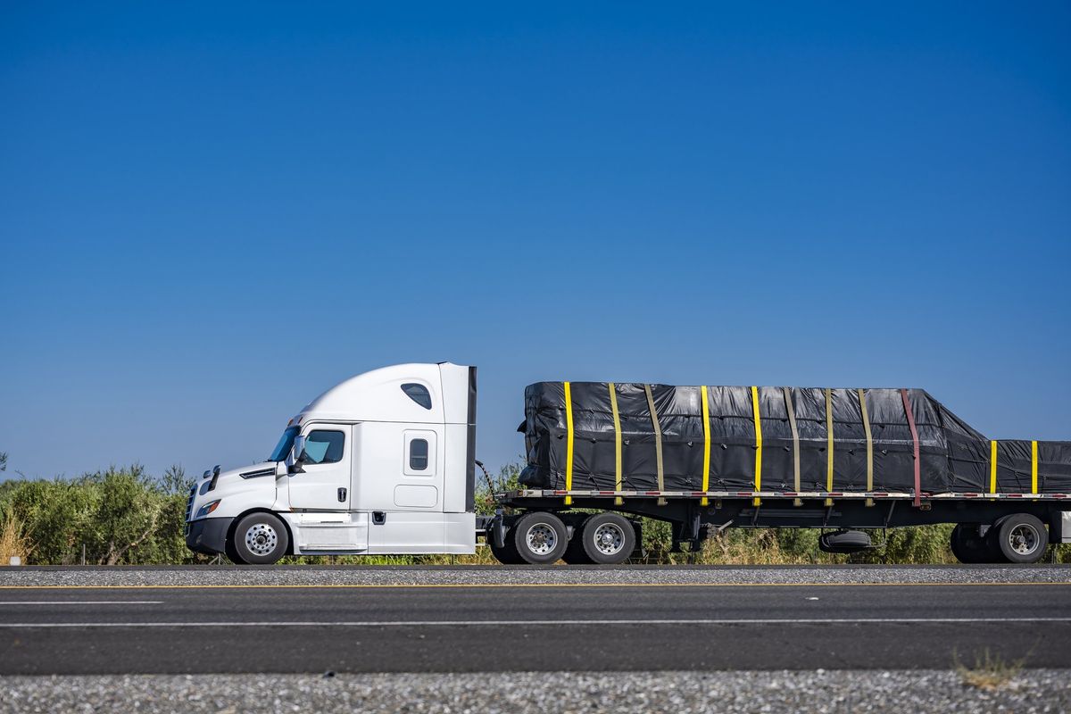 A semi truck on the road with cargo secured to the trailer.