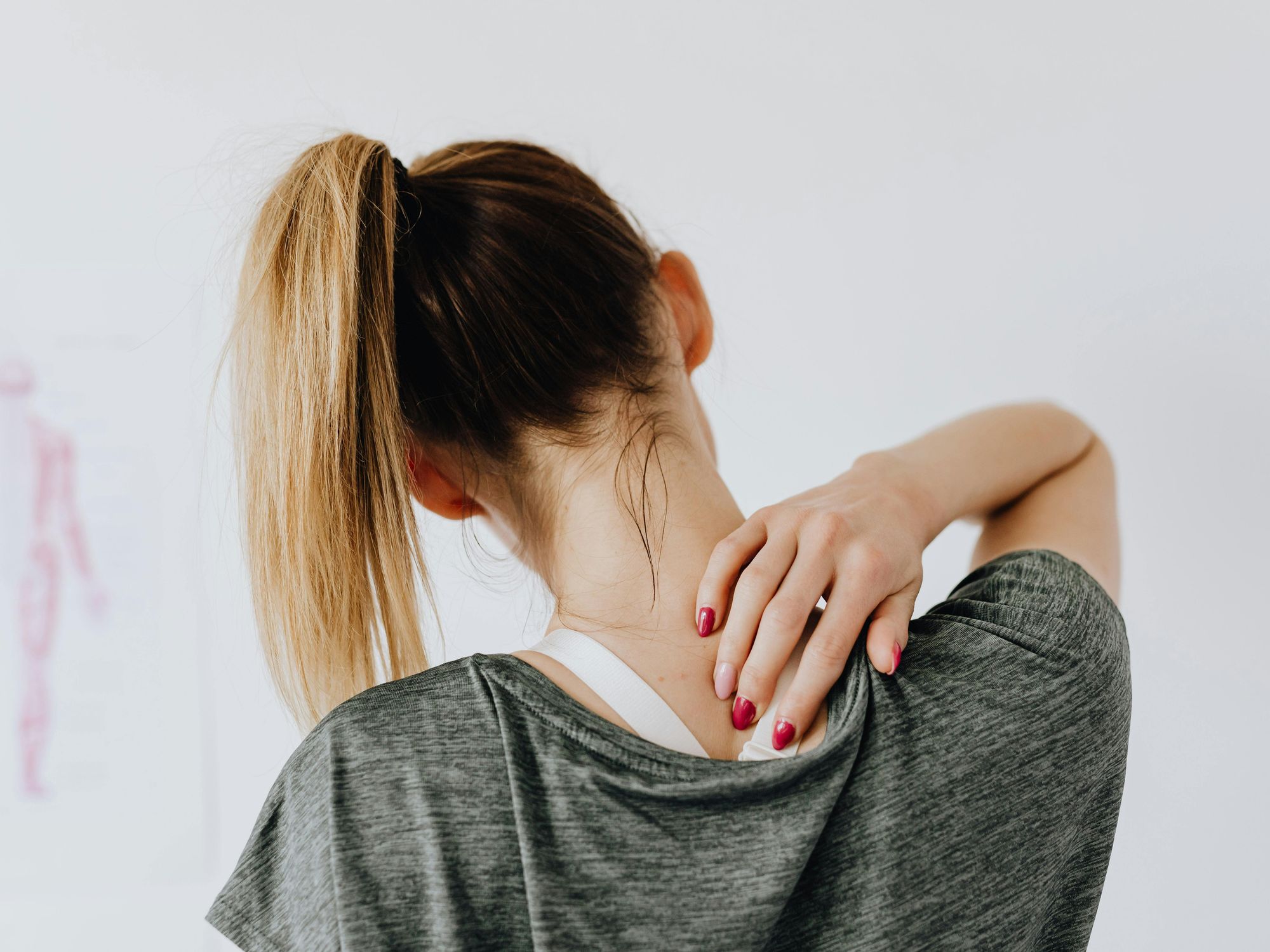 A woman with her back to the camera stretches her neck while massaging the muscles in her back