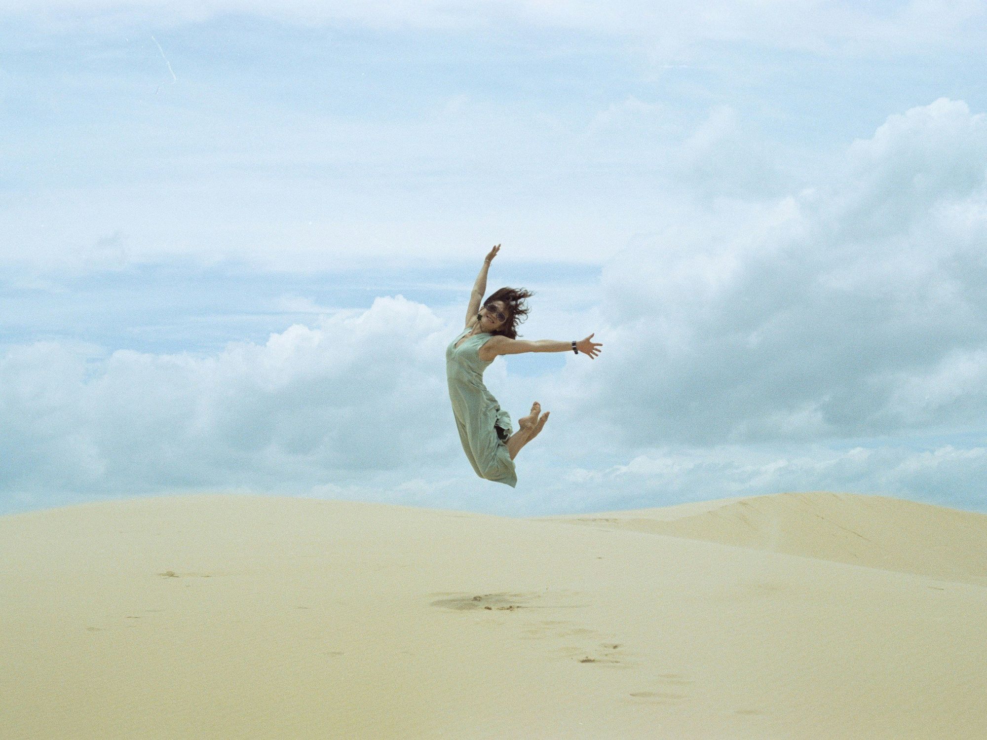 woman in white dress jumping on brown sand during daytime
