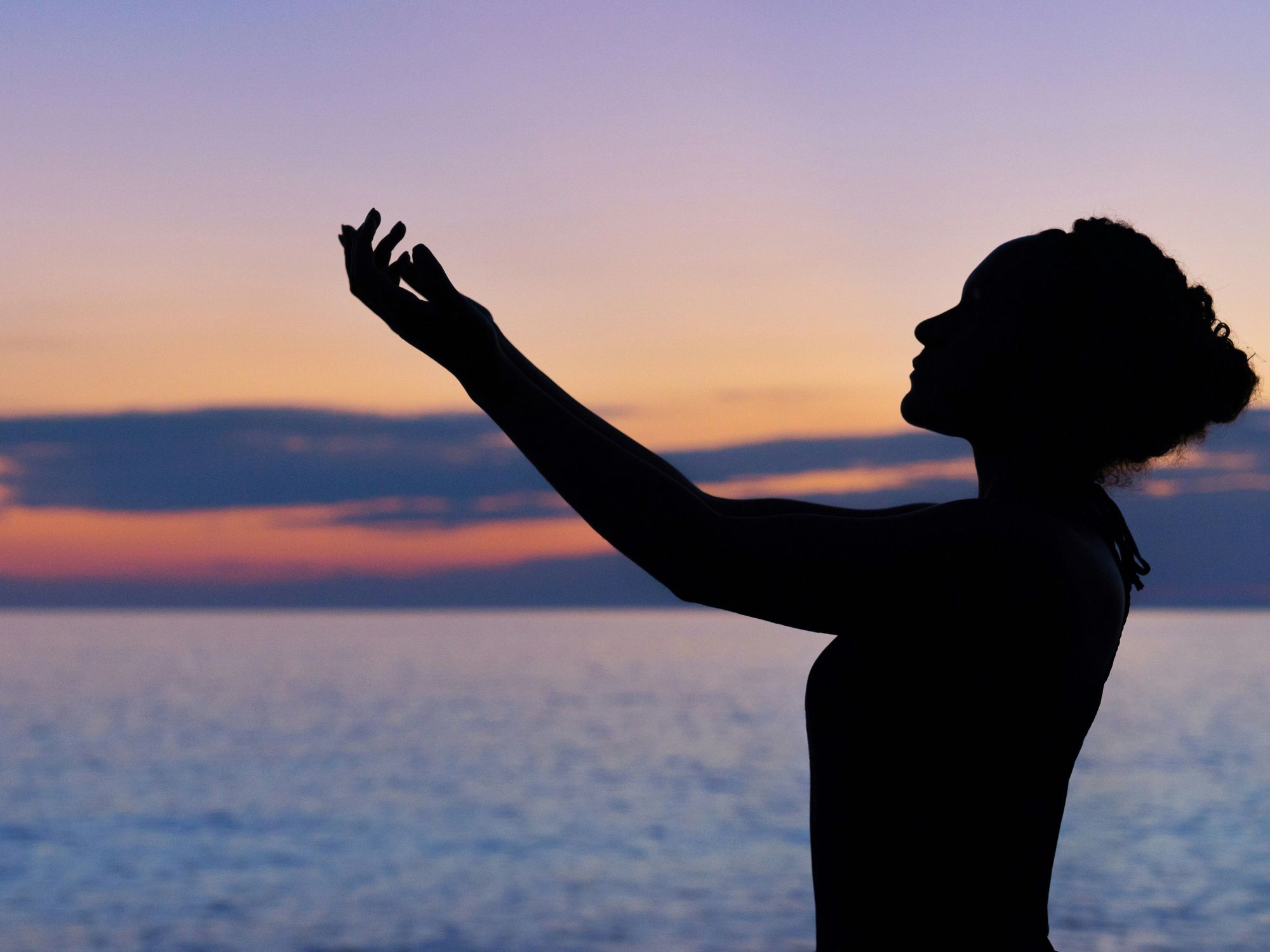 silhouette of woman raising her right hand at sunset